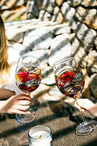 Two people toasting with colorful, artistic wine glasses outdoors.