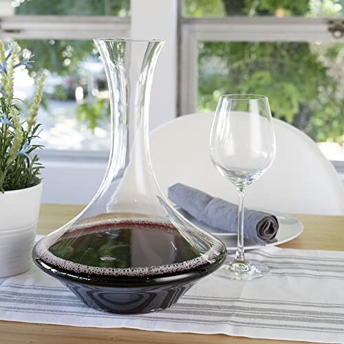 Glass decanter with red wine and a wine glass on a table.