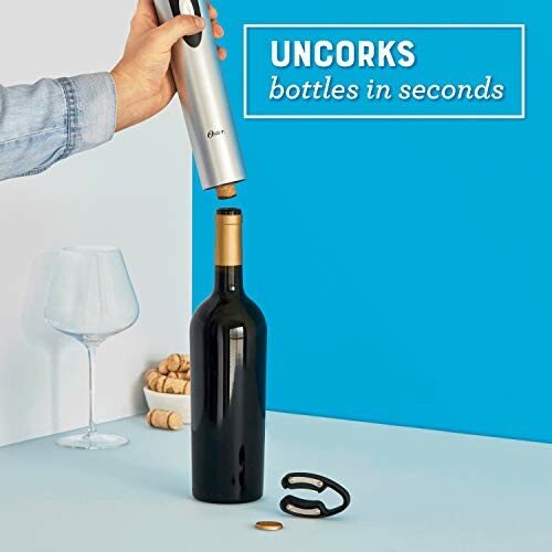 Person using an electric wine opener on a bottle with corks and glass nearby.