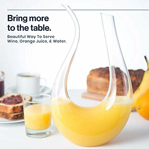 Elegant glass pitcher with orange juice on a table with bread and fruit.