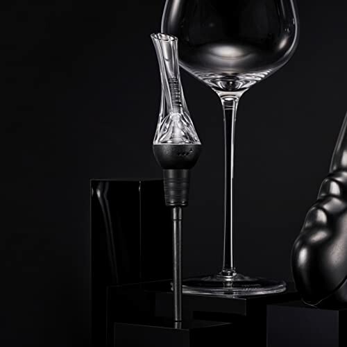 Elegant wine aerator beside a wine glass against a dark background.