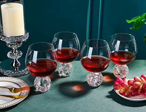 Four wine glasses with red wine on a table with grapes and a candle.