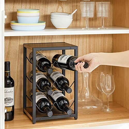 Hand placing wine bottle in black metal wine rack in kitchen cabinet.