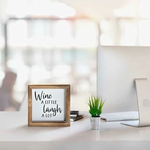 Minimalist desk with framed quote, plant, and computer.