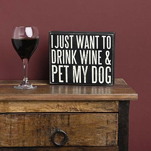 Sign with text 'I Just Want to Drink Wine & Pet My Dog' next to a glass of red wine on a wooden table.