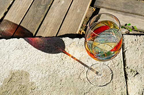 Wine glass casting colorful shadow on stone surface.