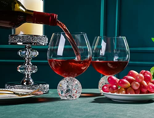 Red wine being poured into elegant glasses with grapes and candle in background.