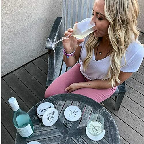 Woman sitting on patio chair drinking wine with coasters on table.